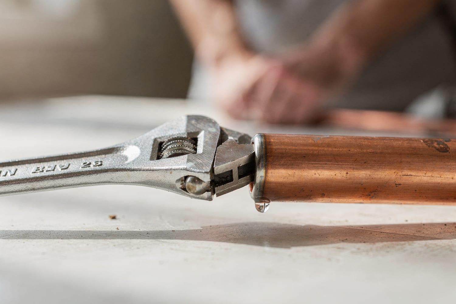 A wrench closing a copper pipe joint, a single drop of water catching the light